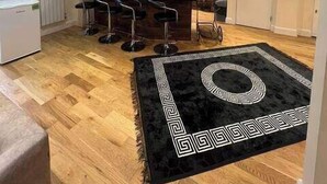 A modern kitchen with a central island, bar stools, and a black rug with a geometric pattern. - 3-Bed Central Apartment - Sleeps 8 & Free Parking (London)