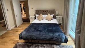 A bedroom with a large bed, two bedside tables, a headboard, and a view of a balcony through a window. - 3-Bed Central Apartment - Sleeps 8 & Free Parking (London)
