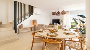 Un salon moderne avec un coin repas, comprenant un escalier, des meubles en osier et une grande fenêtre offrant une vue dégagée.