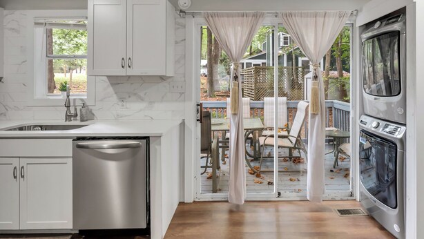 Una cocina moderna con armarios blancos, lavavajillas y horno. Hay una ventana con vistas al exterior.