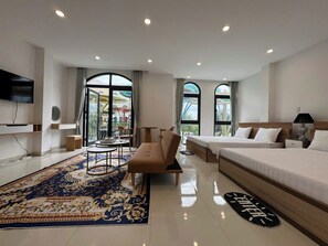 A hotel room with a large bed, a sofa, a small table, and a TV. There are two windows with curtains, and a balcony is visible through the windows. - Gio Bien Homestay - Sea Breeze (Phu Quoc)