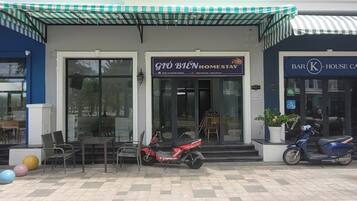 Fachada con un letrero que dice 'GTO BIEN HOMESTAY' y otro que dice 'BAR K HOUSE CAFE'. Hay sillas y una moto estacionada afuera.