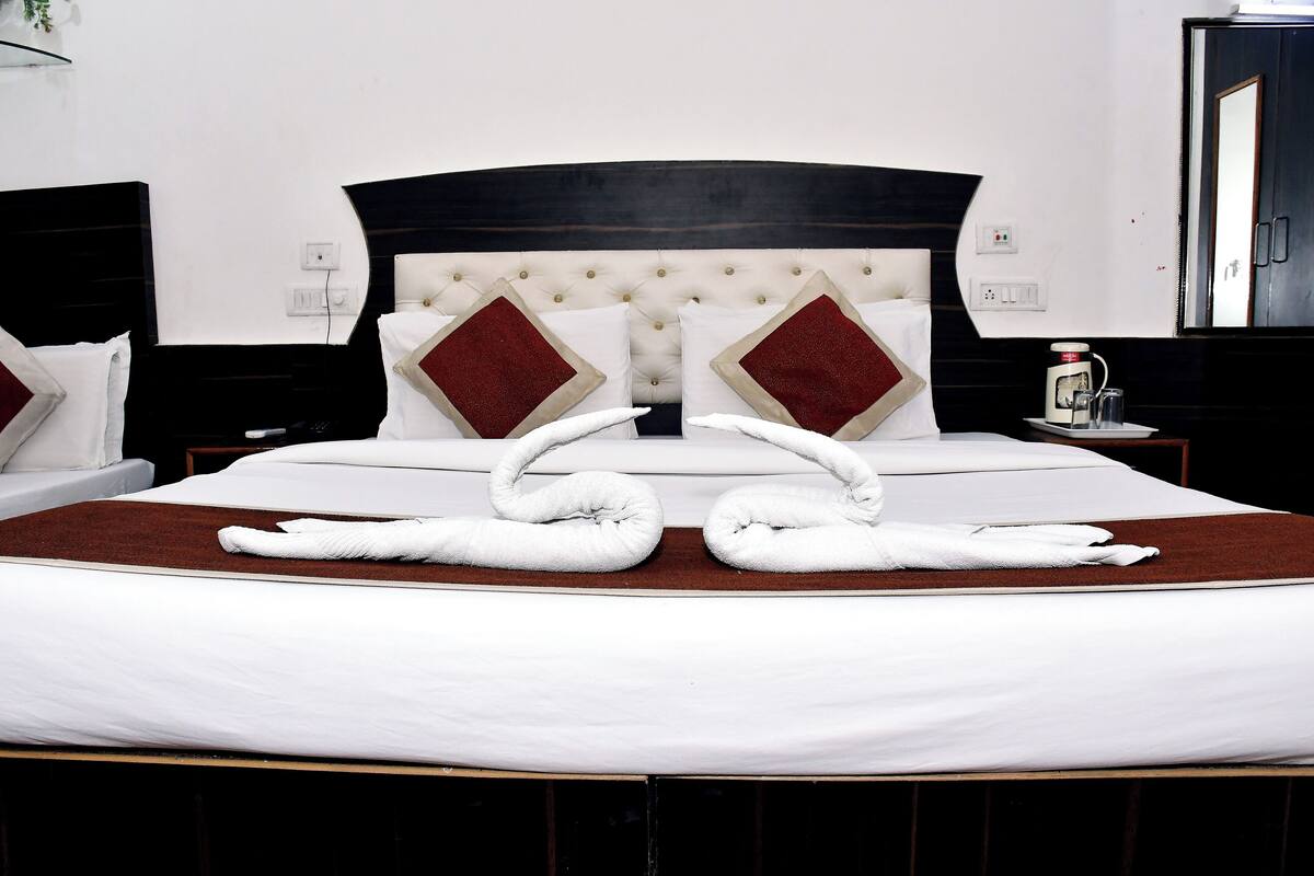 A neatly made bed with two white towels arranged in a decorative manner, a tufted headboard, and a red accent pillow.