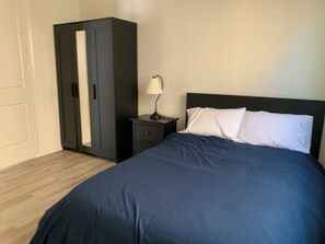 A bedroom with a bed, a nightstand, a lamp, and a wardrobe.