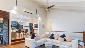 A modern living room with a white sectional sofa, ottomans, and a dining area visible through an open door. - Family-Friendly 3BR Home with Outdoor Living in Ferny Hills (Ferny Hills)
