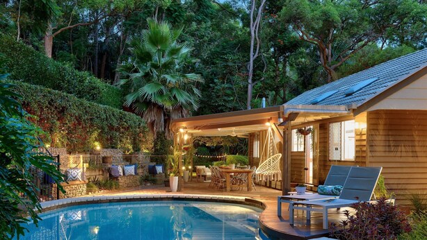 A poolside area with a wooden deck, a covered seating area, and a stone wall. - Family-Friendly 3BR Home with Outdoor Living in Ferny Hills (Ferny Hills)