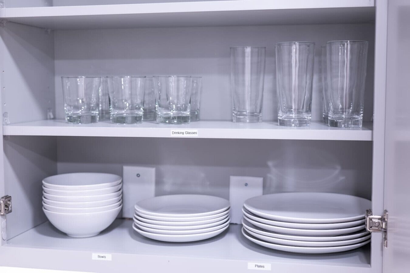 Een kast met planken met drinkglazen, kommen en borden.