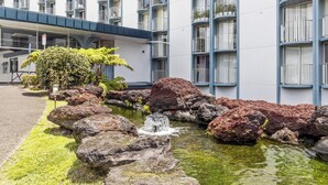 A hotel with a modern design, featuring a landscaped garden with a small pond, rocks, and a waterfall. - Hilo Getaway: 2BR Condo w/ Pool, A/C & Incredible Views (Hilo)