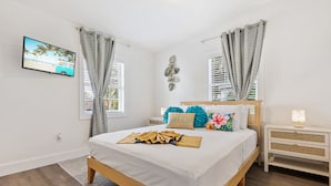 A bedroom with a wooden bed, white bedding, a TV on the wall, and a nightstand with a lamp. - Oasis Paradise/Pool/Mini Golf/Exquisite Escape Sunset/Centric (Port Charlotte)