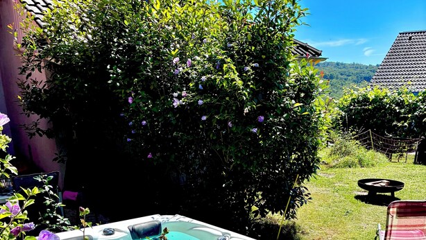 A hot tub in a garden with a grassy area, a chair, and a fence. - Peace & relaxation in the countryside! Mediterranean country house apartment with jacuzzi (Merchweiler)