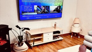 A living room with a flat-screen TV mounted on the wall displaying a sports news channel. - Peace & relaxation in the countryside! Mediterranean country house apartment with jacuzzi (Merchweiler)