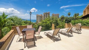 A rooftop patio with a table and chairs, surrounded by greenery and overlooking a cityscape with high-rise buildings. - Studio Apt. Just 5-mins Walk from Flamingo Beach! (Playa Flamingo)