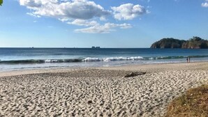 A beach with a sandy shore, waves, and a distant rocky outcrop. - Studio Apt. Just 5-mins Walk from Flamingo Beach! (Playa Flamingo)