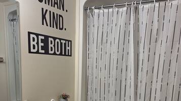 Ein Badezimmer mit Waschbecken, Toilette und Badewanne. An der Wand ist ein motivierendes Zitat und auf der Ablage steht eine kleine Pflanze.