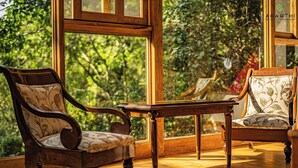 A room with two wooden chairs, a wooden table, and large windows offering a view of greenery. - Agarthi (Cintalapa)