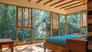 A bedroom with a large window, wooden furniture, and a view of a forest. - Agarthi (Cintalapa)