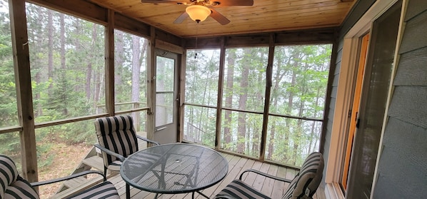 A covered porch with a table and chairs, large windows, and a ceiling fan. - Northwoods Lakefront Paradise, 2-bedroom Cabin on the Beautiful Minong Flowage! (Minong)