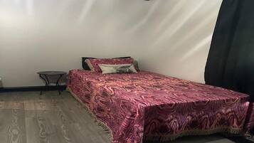 A bedroom with a bed, a small table, and a curtain.