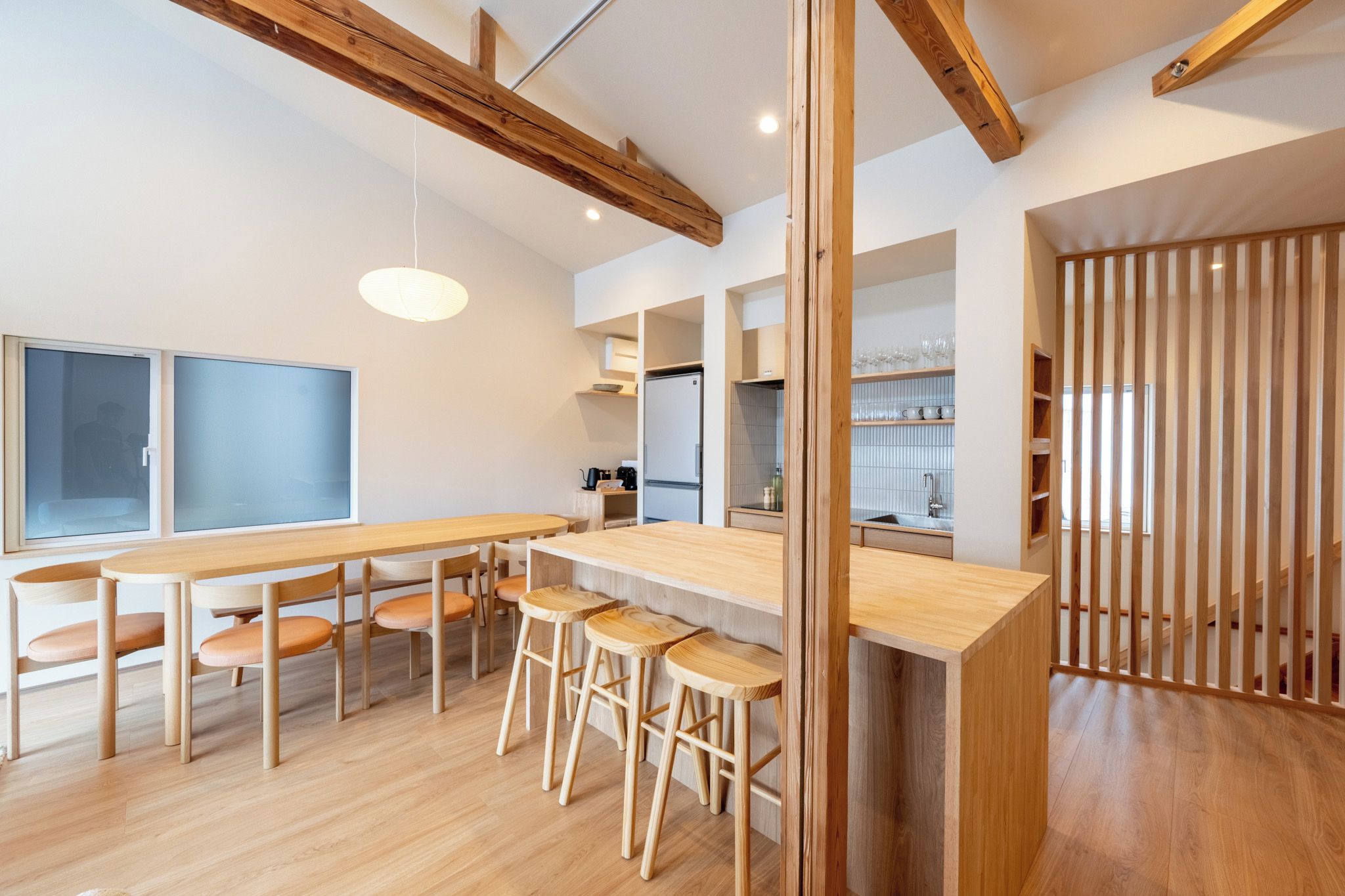 A modern kitchen with wooden beams, a central island, bar stools, and a view into the dining area.