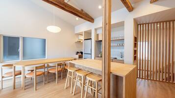 A modern kitchen with wooden beams, a central island, bar stools, and a view into the dining area.