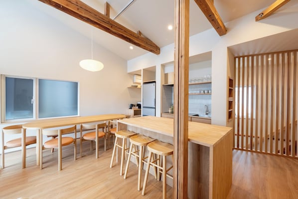 A modern kitchen with wooden beams, a central island, bar stools, and a view into the dining area. - Bonbori (Nozawaonsen)