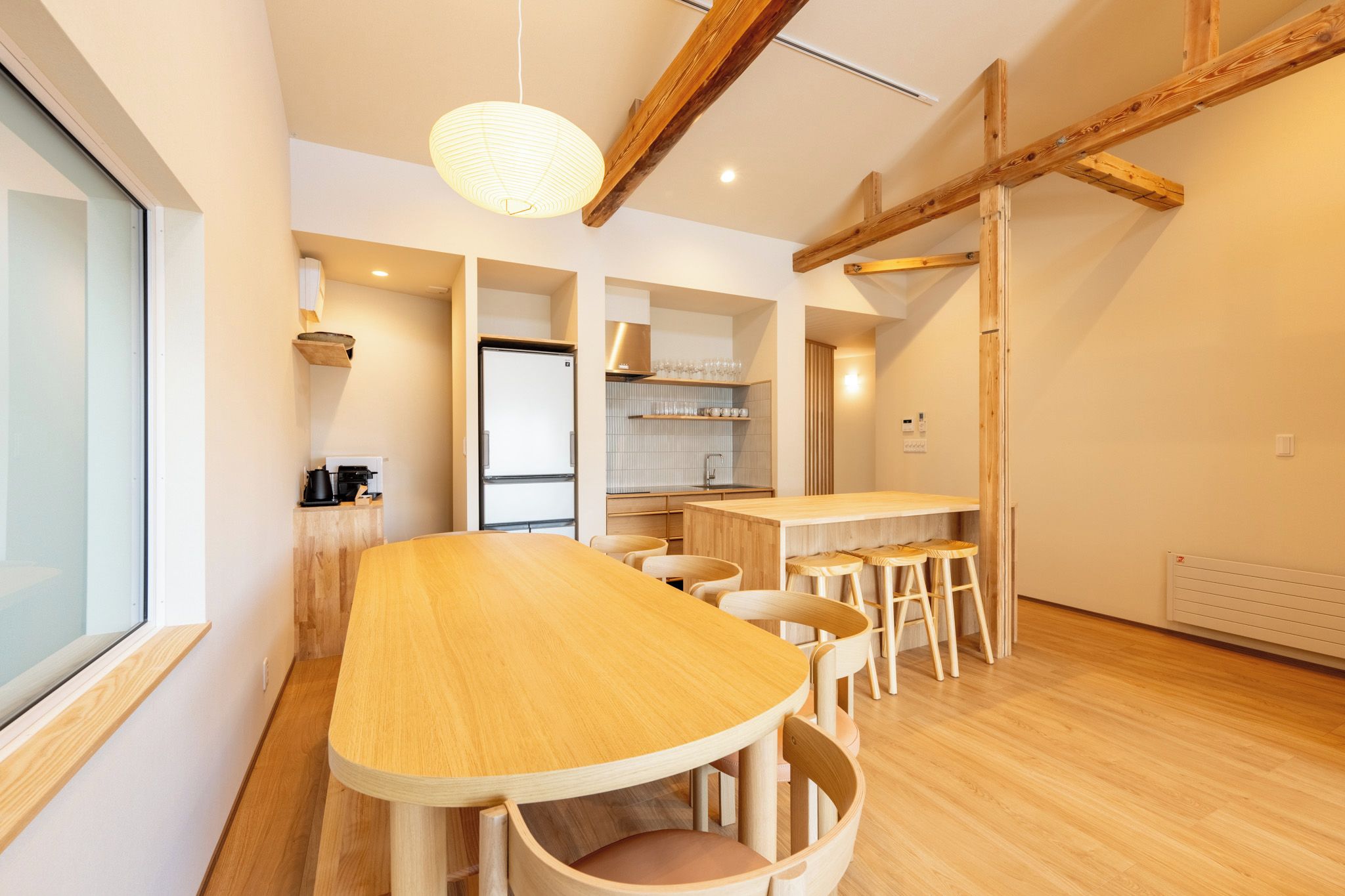 A modern kitchen with a wooden table and chairs, a hanging light fixture, and a view of the adjacent living area.