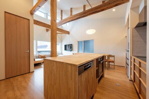 A modern kitchen with wooden beams, a central island with a dishwasher, and a dining area with a TV.