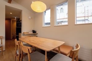 A dining area with a wooden table and chairs, a hanging light fixture, and a view of the street through windows. - Bonbori (Nozawaonsen)