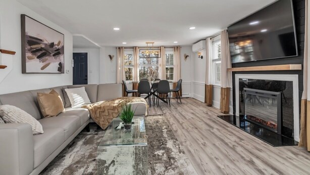A modern living room with a sofa, coffee table, and a fireplace. There is a dining area with a table and chairs in the background. - Unique 4bedrooms 2 bathrooms stunning getaway unit (Methuen)