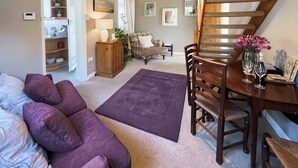 A living room with a sofa, a dining table with chairs, a staircase, and a kitchen area in the background.