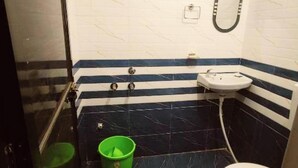 A bathroom with a shower, a sink, a toilet, and a green bucket. - Hotel MP Katra (Katra)