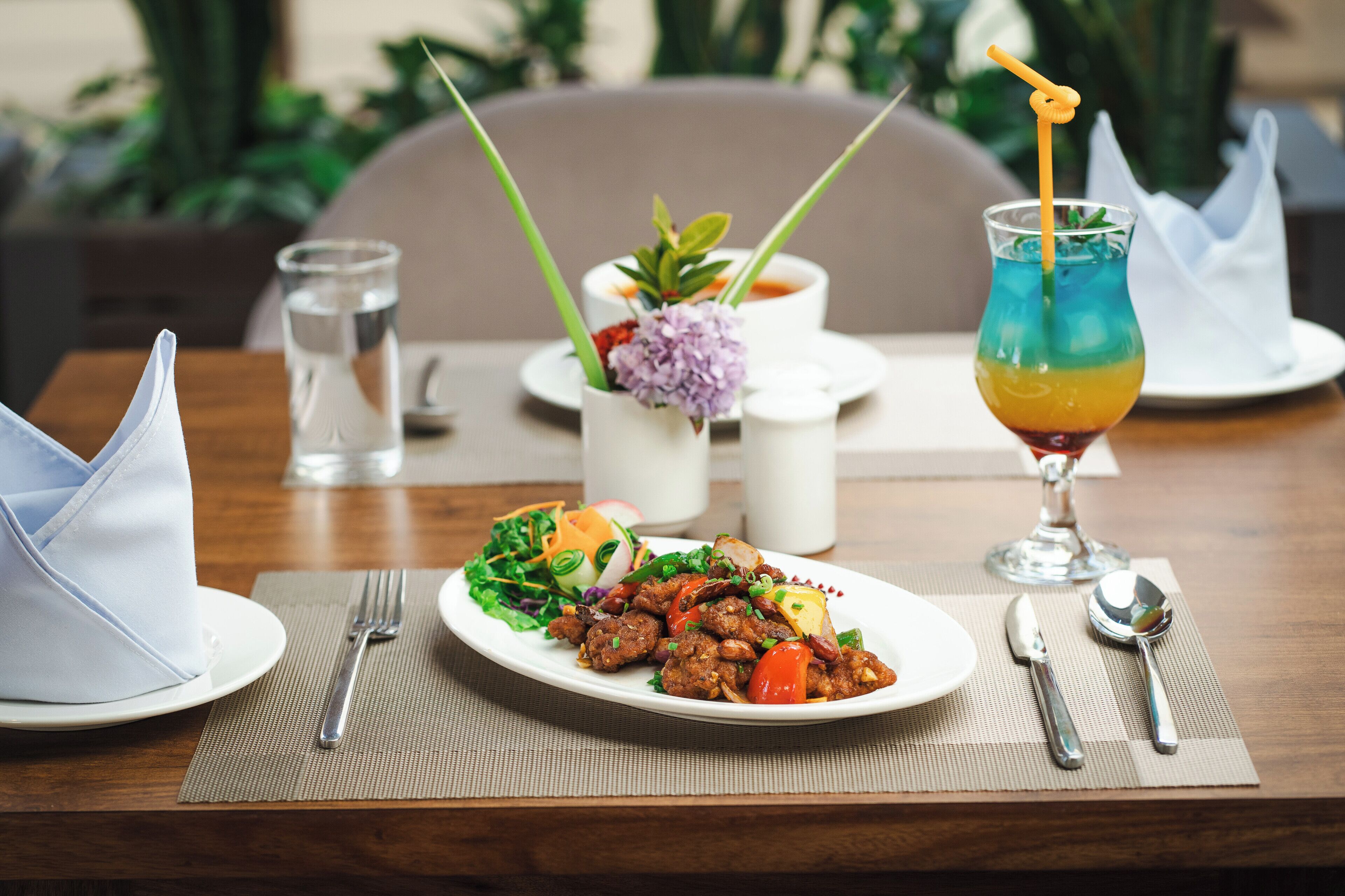A dining table with a plate of food, a glass of drink, and a small vase with flowers.