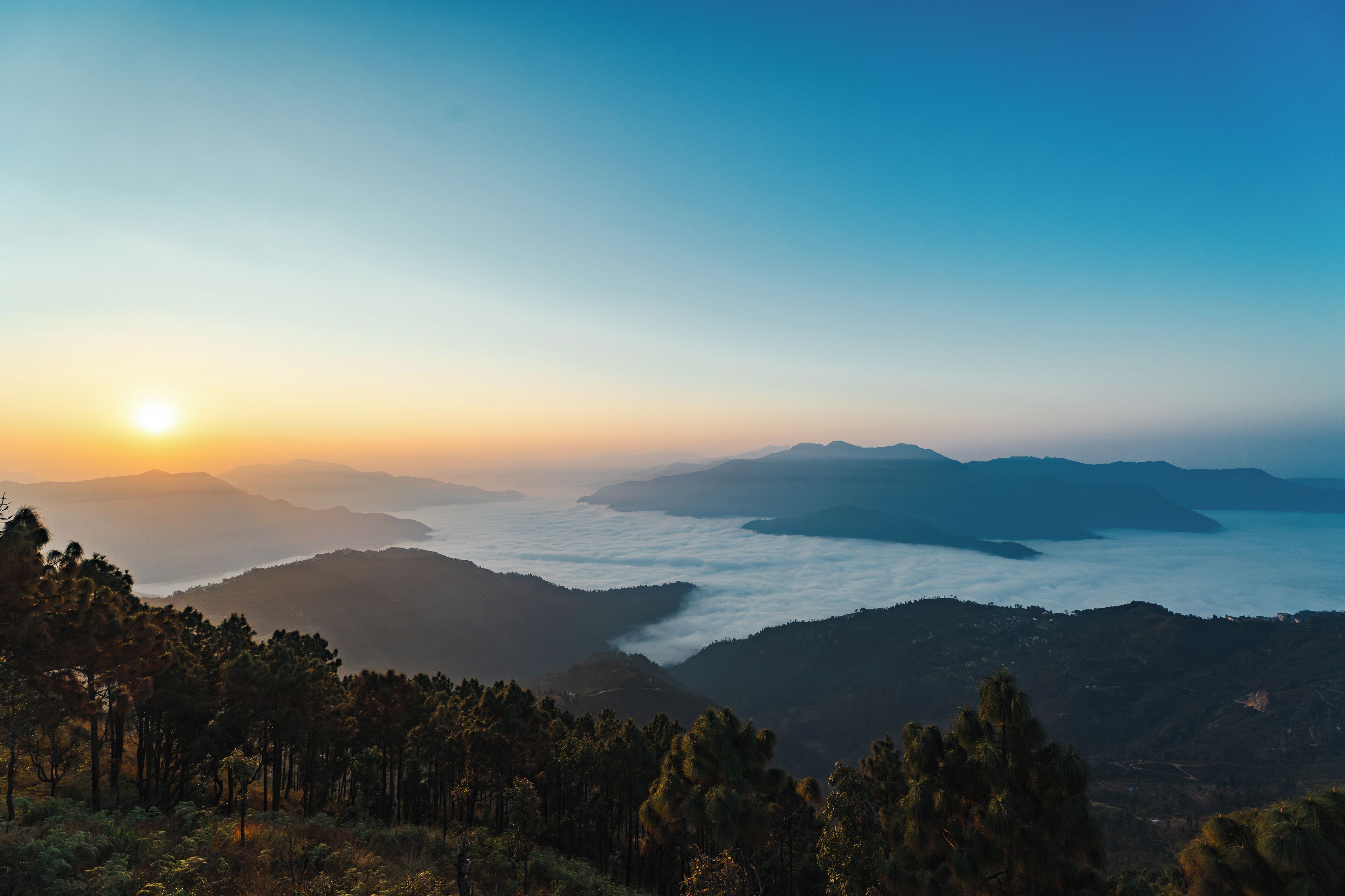 Eine Berglandschaft mit Sonnenaufgang oder Sonnenuntergang, bewaldete Hügel und ein Tal darunter.