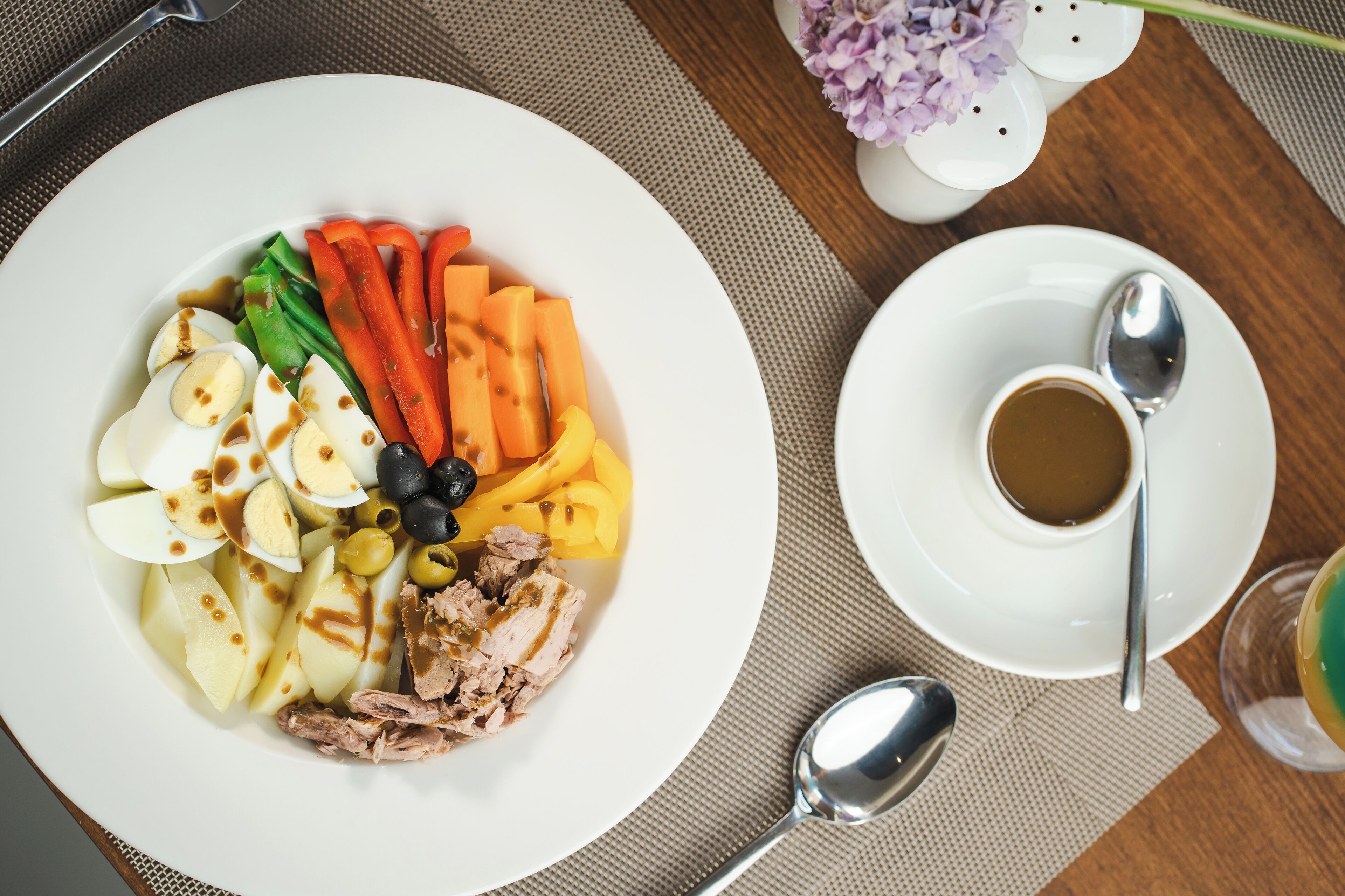 Un plato de comida con diversos vegetales y carne, una taza de café y una cuchara sobre una mesa.