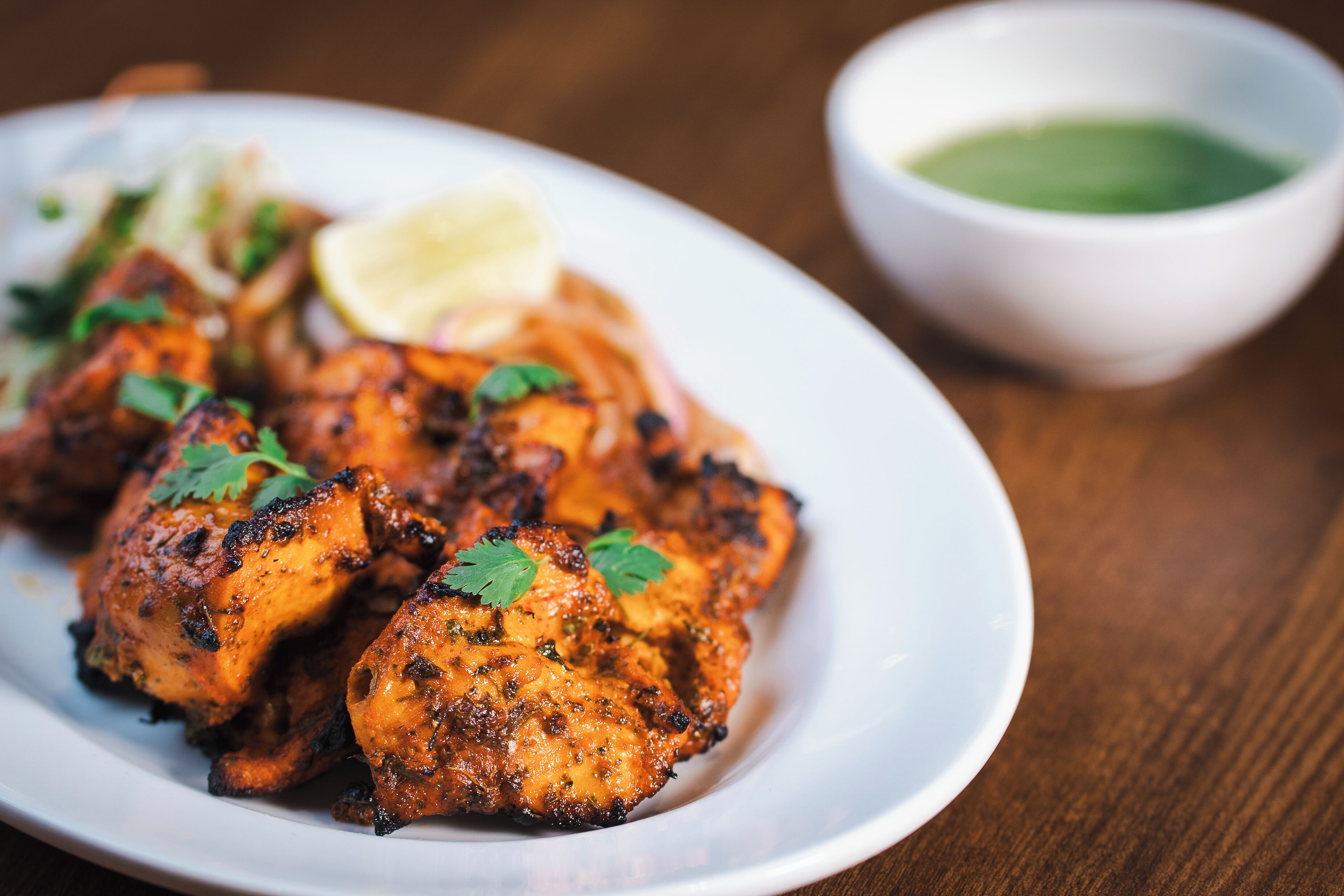 A plate of grilled chicken with a side of sauce and a lemon wedge.