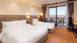 Habitación de hotel con dos camas, un escritorio, una silla y un balcón con vistas.