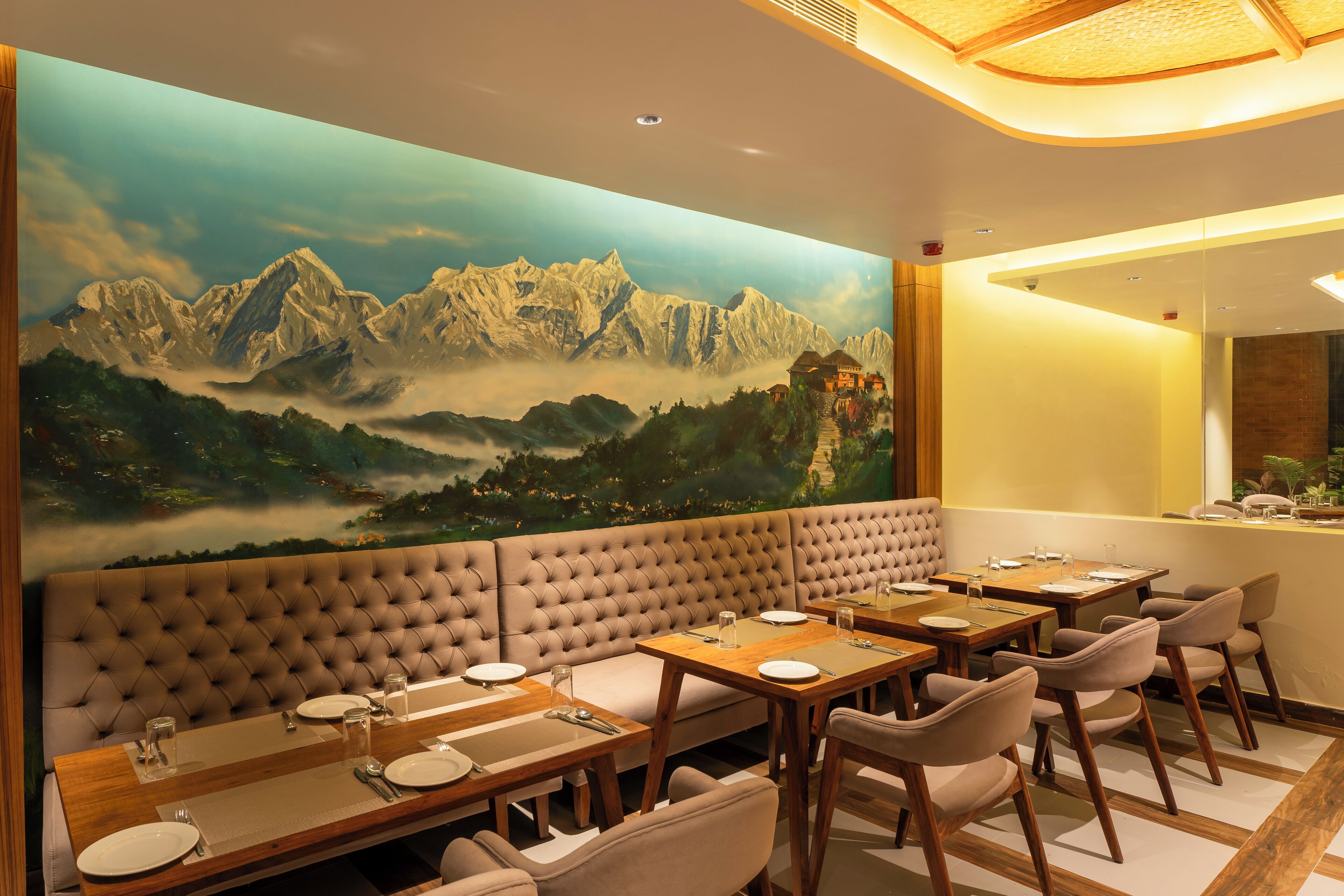 A restaurant with a large mural of mountains, a tufted bench seating area, and wooden tables with chairs.