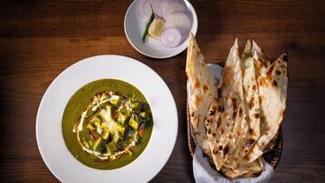 A plate of green curry with naan bread and a bowl of sliced onions and a lemon.