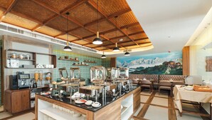 Montaje de bufé con distintas estaciones de comida, una máquina de café y disposición de mesas.