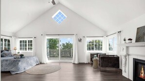 A spacious bedroom with a large window, a fireplace, and a balcony.
