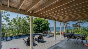 A covered outdoor deck with a hot tub, seating area, and a view of the sea.