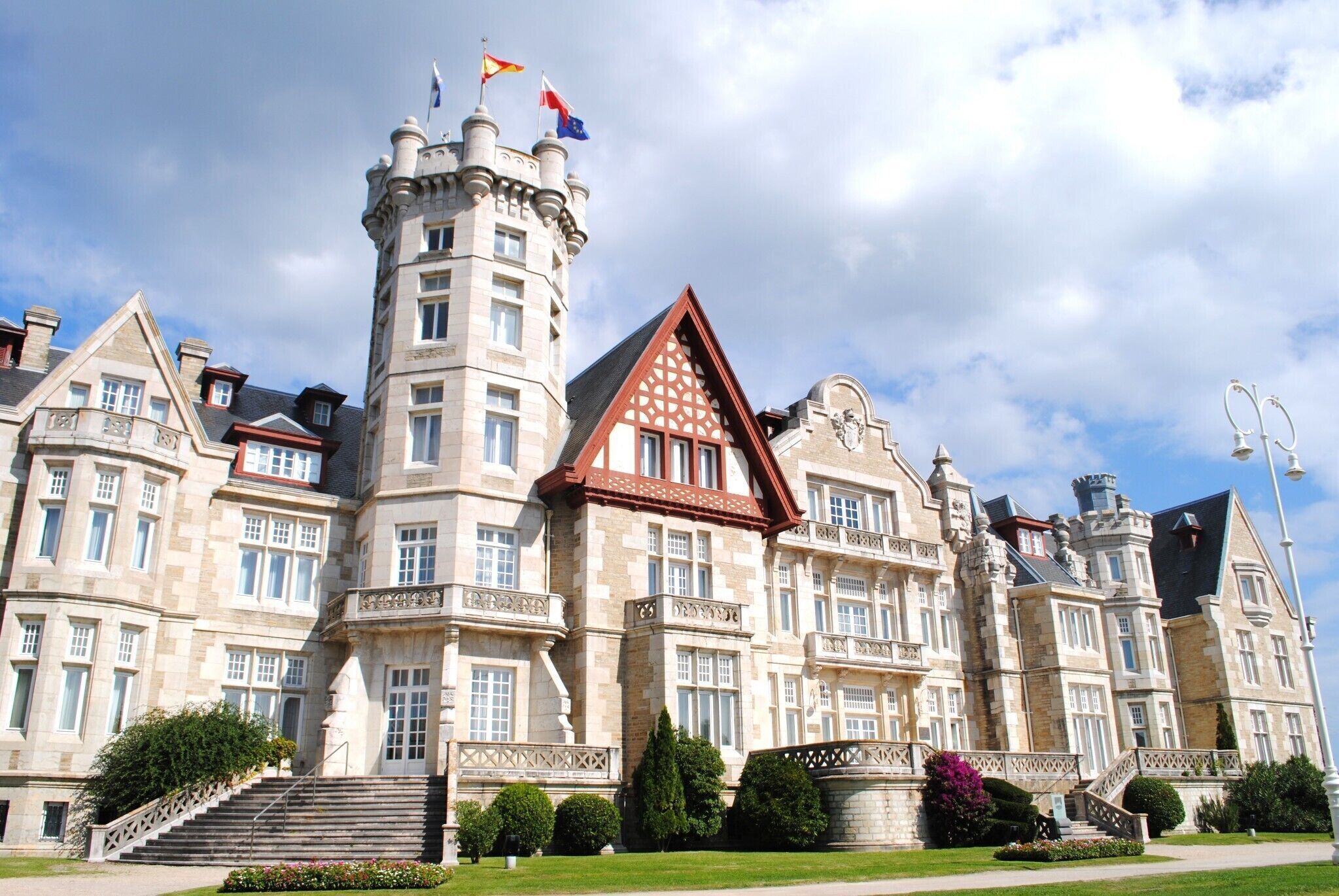 Um edifício grande e histórico com uma torre imponente, várias janelas e um gramado bem cuidado.