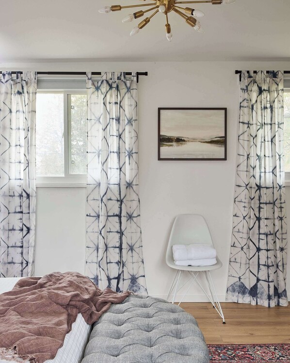 A bedroom with a bed, a chair with a towel, a window with curtains, and a ceiling light fixture.