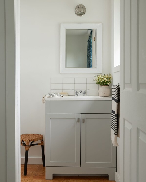 A bathroom with a white vanity, a mirror, a sink, a potted plant, and a striped towel.