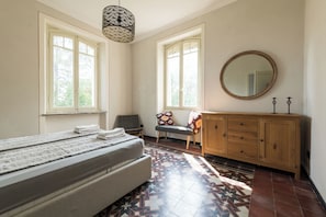 A bedroom with a bed, a chair, a dresser, and a large mirror.