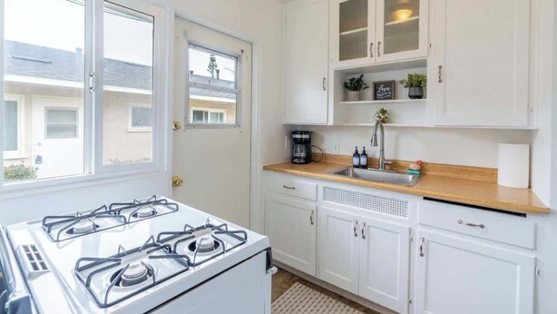 Una cocina moderna con armarios blancos, una estufa a gas, un lavamanos y una ventana con vistas al exterior.