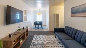 Una sala de estar moderna con un televisor de pantalla plana grande, un sofá azul oscuro, un mueble de entretenimiento de madera y una alfombra estampada.