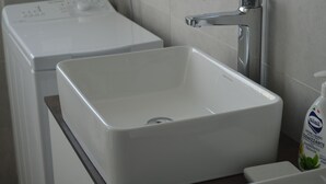 Un baño moderno con un lavamanos blanco, un grifo y una lavadora al fondo.