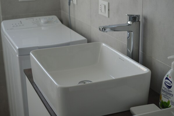 Un baño moderno con un lavamanos blanco, un grifo y una lavadora al fondo.