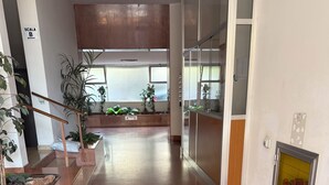 Un pasillo amplio con piso pulido, plantas en macetas y una escalera que lleva a un nivel superior.